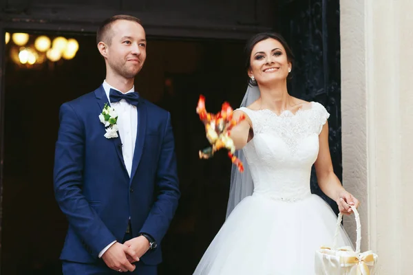 Nevěsta hází sladkosti stojící ženich v vchodu — Stock fotografie