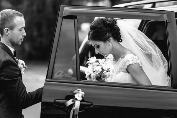 Groom ajuda noiva a sair do carro preto — Fotografia de Stock