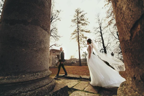 Vento sopra o vestido da noiva enquanto ela caminha atrás de uma catedra arruinada — Fotografia de Stock