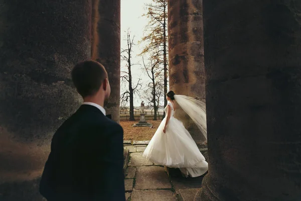 Groom observa uma noiva enquanto o vento sopra seu véu ao redor da pilla — Fotografia de Stock