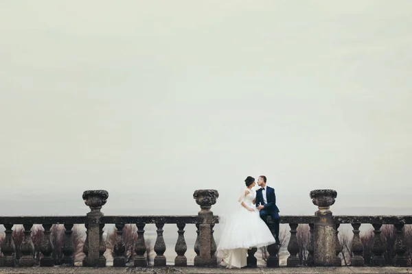 Mariée et marié assis sur le balcon en pierre avec un ciel de couleur profonde — Photo