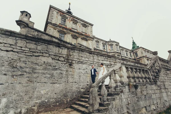 Приголомшливі молодята йдуть сходами зі старого замку — стокове фото