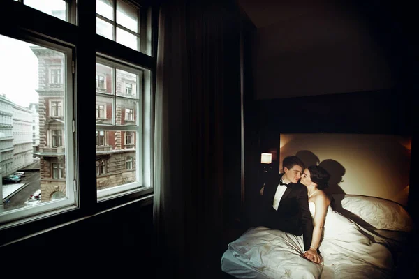 Bride and groom sit on the bed in a dark room — Stock Photo, Image