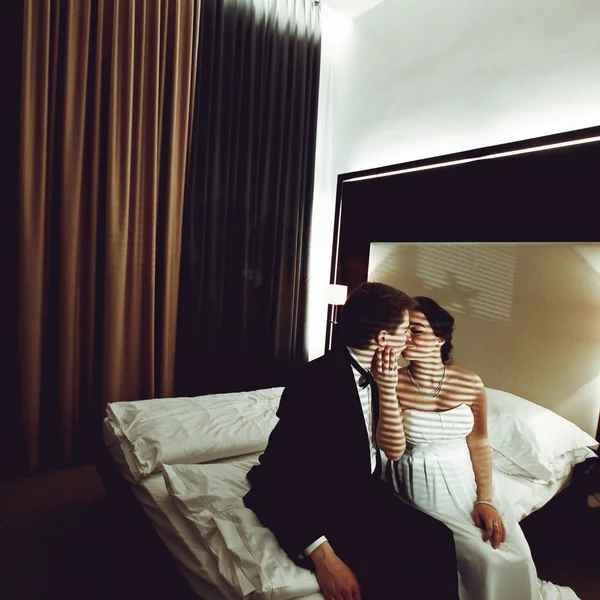 Noiva beija um noivo sentado com ele em uma cama — Fotografia de Stock