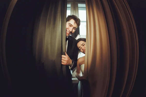 Bruid grimaces permanent achter het gordijn met een bruidegom — Stockfoto