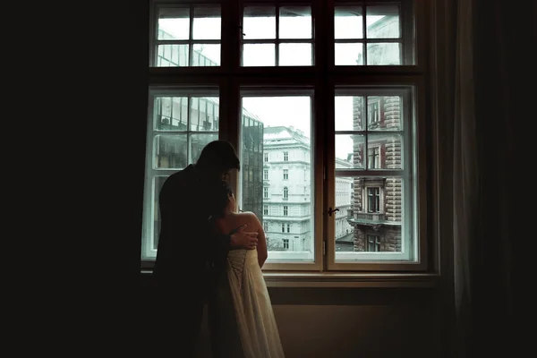Noiva se inclina para um noivo olhando com ele através da janela em th — Fotografia de Stock