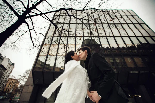 Newlyweds kiss under a huge glass building — Stock Photo, Image