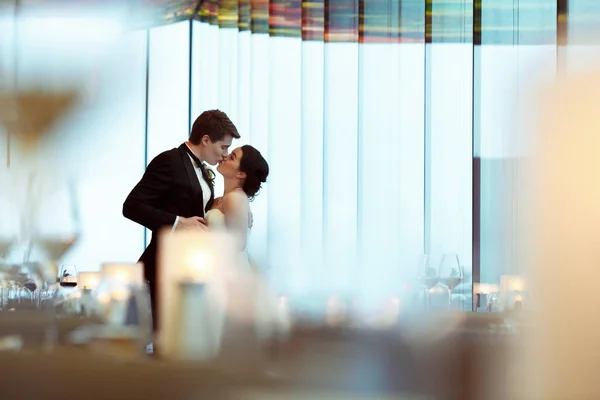Um olhar do vidro em um casal de casamento beijando de pé i — Fotografia de Stock