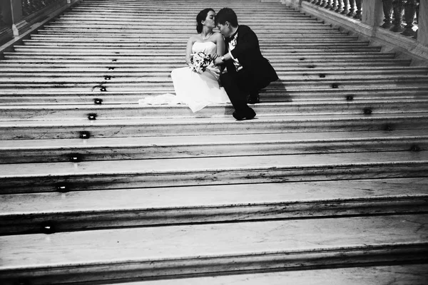 Groom kisses bride's shoulder sitting with her on the marble sta — Stock Photo, Image