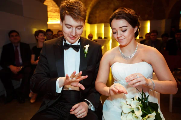 Los recién casados sonrientes miran sus anillos sentados en el restaurante —  Fotos de Stock