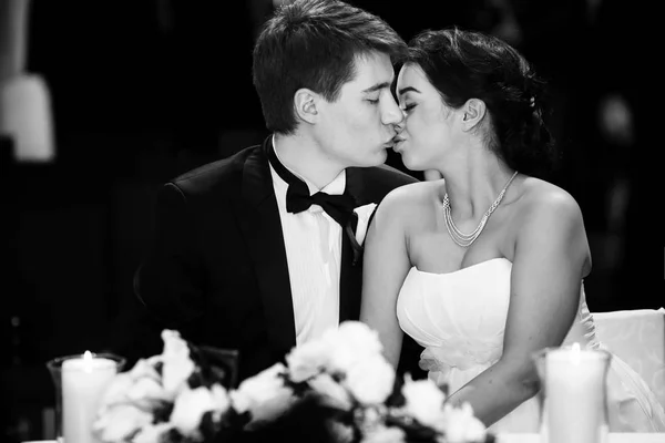 Bride and groom kiss tender sitting at the dinner table — Stock Photo, Image