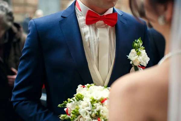 Bruidegom in blauwe pak en rode vlinderdas staat aan de voorkant van een brid — Stockfoto