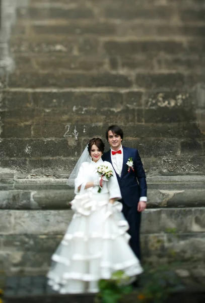 Красивая свадебная пара позирует на перевале за старой серой стеной — стоковое фото
