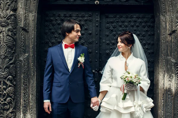 Happy newlyweds hold each other hands standing in the old stone — Stock Photo, Image