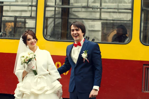 Жених искренне улыбается, стоя с невестой за трамваем. — стоковое фото