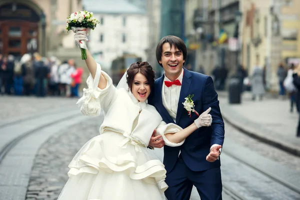 Невеста держит большие пальцы вверх, стоя за женихом на городской площади — стоковое фото