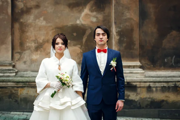 Newlyweds look seriously standing behind an old cathedral — Stock Photo, Image