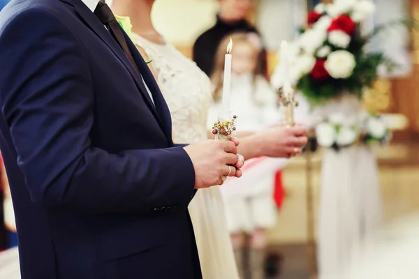 Newlyweds stand straight with white candles in their arms during — Stock Photo, Image