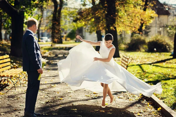 Bride spreads her dress while dancing in the park — Stock Photo, Image