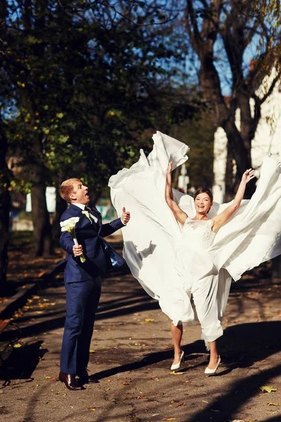 Bride and groom look funny jumping up in the park — Stock Photo, Image