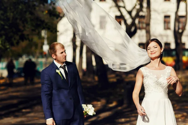 Il sole splende sul viso della sposa mentre il vento le soffia il velo su un groo — Foto Stock