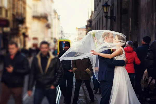 Le vent couvre les jeunes mariés avec un voile pendant qu'ils se tiennent dans la rue — Photo