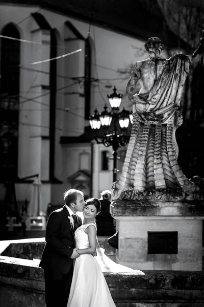 Foto in bianco e nero di sposi che si baciano dietro una statua di — Foto Stock