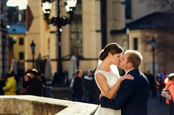 Groom beija uma noiva de pé aos raios de sol em um citysquare — Fotografia de Stock