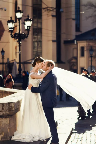 Vento soffia velo della sposa via mentre lei sta in abbracci dello sposo — Foto Stock