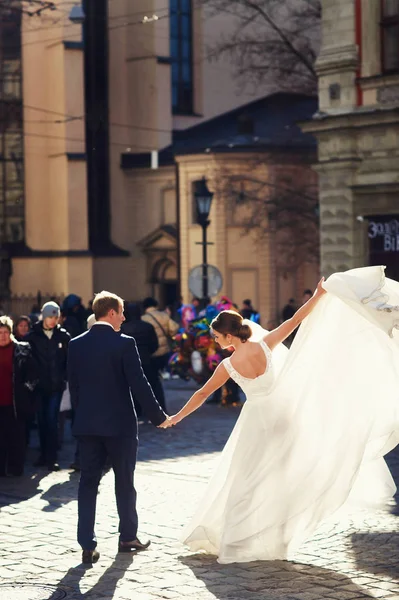 Sposa alza il vestito tenendo la mano dello sposo mentre in piedi su — Foto Stock