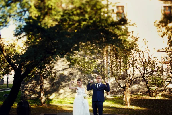 Bride and groom show their strong muscles posing on the green ba — Stock Photo, Image