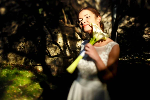 Bride touches her face with a tender bouquet of callas standing — Stock Photo, Image