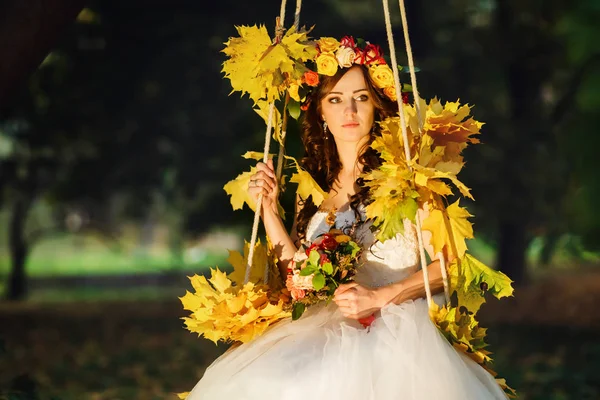 Herbstsonne scheint über die atemberaubende Braut, während sie auf einem Swin sitzt — Stockfoto