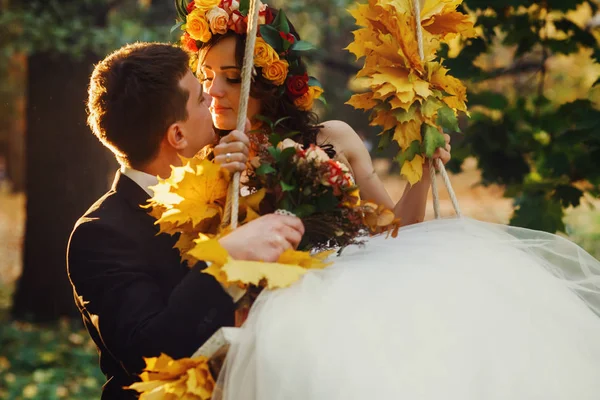 Groom tient une mariée dans une balançoire décorée de feuilles jaunes tombées — Photo