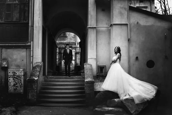 Braut steht auf den Steinen und breitet ihr Kleid aus, während der Bräutigam geht — Stockfoto