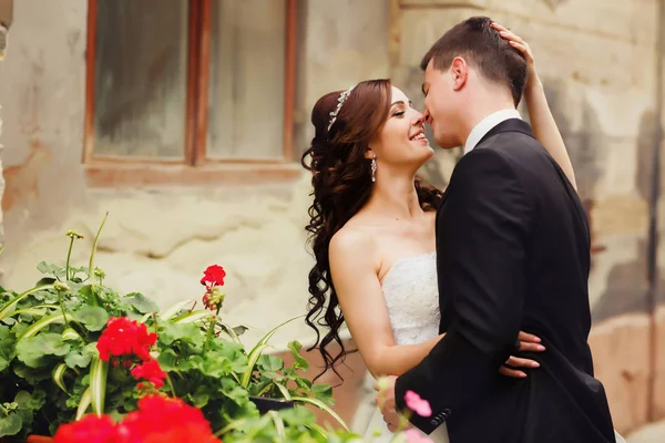 Sonriente novia sostiene la cabeza del novio mientras él la besa detrás de una re — Foto de Stock