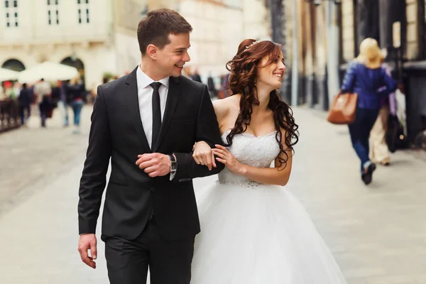 Smiling newlyweds walk along the street looking at old buildings — Stock Photo, Image
