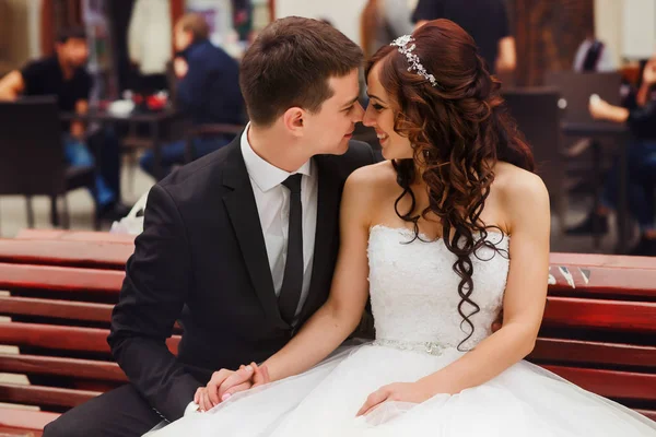 Bonita sonrisa de recién casados sentados en el banco en una plaza de la ciudad — Foto de Stock