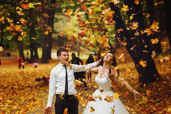 Mariée et marié thow les feuilles jaunes vers le haut dans l'air — Photo