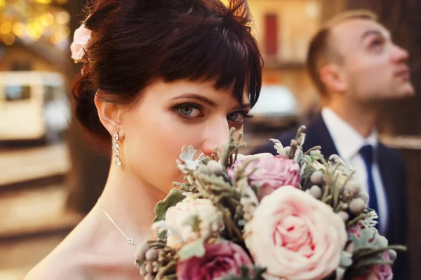 青い目のブルネット花嫁がウェディング ブーケの背後にある彼女の顔を非表示に — ストック写真