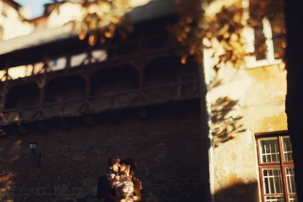 Sposa e sposo bacio in piedi sotto un vecchio balcone di legno — Foto Stock