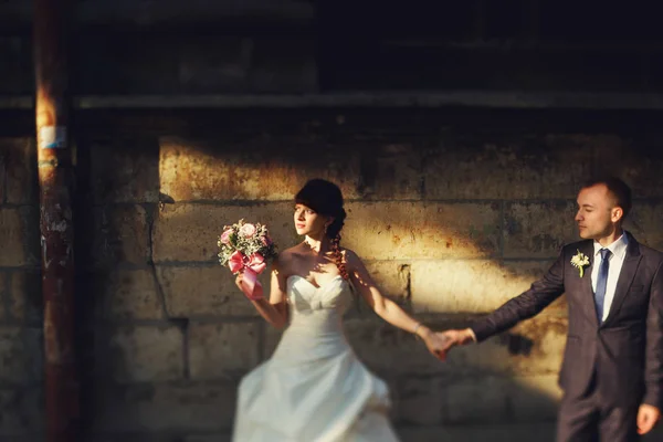 La mariée regarde un soleil tenant un bouqet dans le han d'un bras et d'un marié — Photo