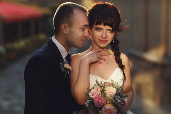 Sorridente sposo si appoggia ad una splendida sposa bruna in piedi sul — Foto Stock