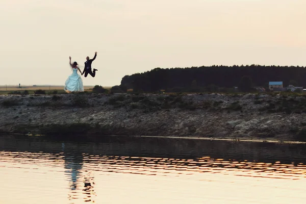 Щасливі молодята стрибають на березі озера — стокове фото