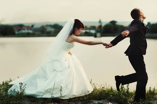 Vőlegény menyasszony kezemet, szorosan a tó parton fut — Stock Fotó