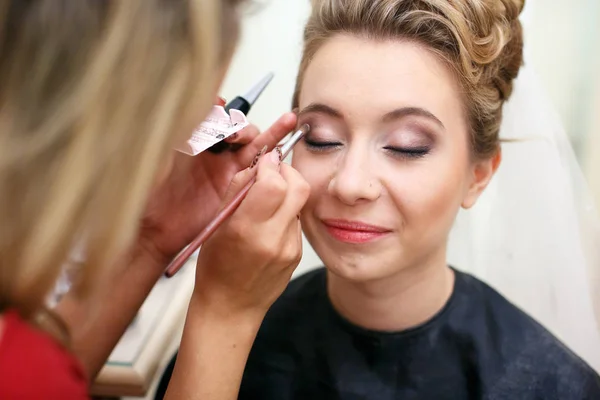 Bride smiles while artist puts the eyeshadows under her brows
