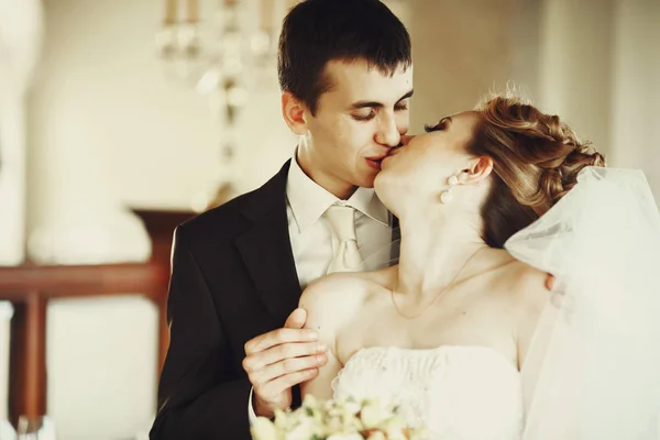 Ženich líbá nevěstu, stojící za ní v hotelové hale — Stock fotografie