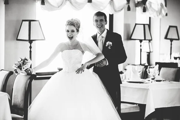 Alegre recién casados de pie riendo en una sala de restaurante vacía —  Fotos de Stock