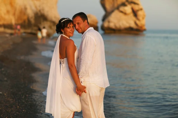Sposa e sposo guardano oltre le spalle in piedi sulla riva del mare — Foto Stock