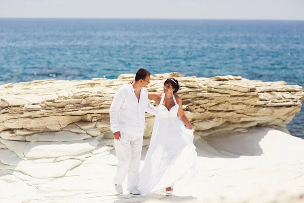 Groom segura a cintura da noiva enquanto caminham ao longo da costa do mar de pedra — Fotografia de Stock